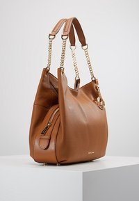 Sac à main en cuir marron avec finition texturée, quincaillerie dorée, doubles anses et poche zippée sur le côté. Présente un accent de logo.