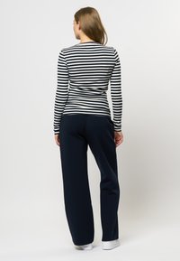 Langermet topp i marineblå og hvite striper med en tettsittende silhuett, kombinert med marineblå løse bukser. Glatt stoff og enkelt design.