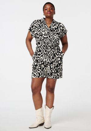 Robe à manches courtes à motifs noir et blanc avec un col, taille cintrée et poches latérales, complétée par des bottes de cowboy blanches.