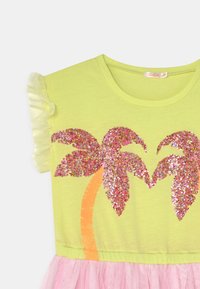 Żółta koszulka z okrągłym dekoltem, krótkimi falbankowymi rękawami, zdobiona różowymi, błyszczącymi palmami i pomarańczowym pniem. Dołączona różowa spódnica z tiulu.