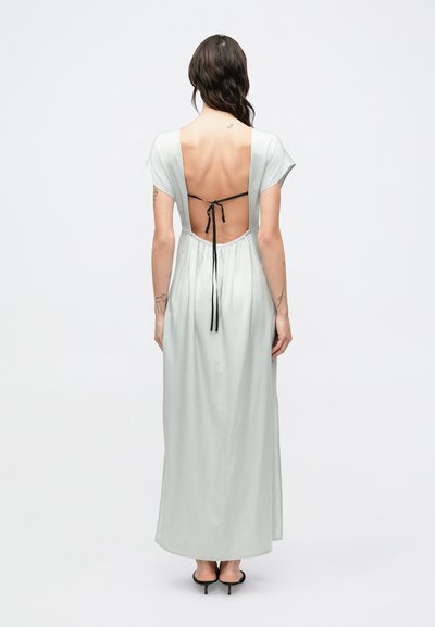 Dlhé svetlozelené šaty s hlbokým výstrihom na chrbte, krátkymi rukávmi a čiernou stuhou v páse. Hladká látka s minimálnymi dizajnovými prvkami.