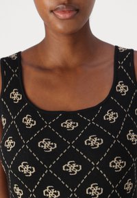 Gros plan d'une personne portant un haut noir sans manches avec un motif entrelacé beige et un col en U.