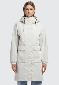Parka leggera di colore crema con cappuccio, polsi elasticizzati, due tasche frontali e dettagli con cordino. Tessuto liscio, design lungo fino al ginocchio.