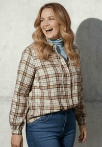 Geruite flanellen shirt in crèmekleurige, bruine en tan tinten met knoopsluiting. Draag het over een lichtblauwe turtleneck met lange mouwen en een ontspannen pasvorm.