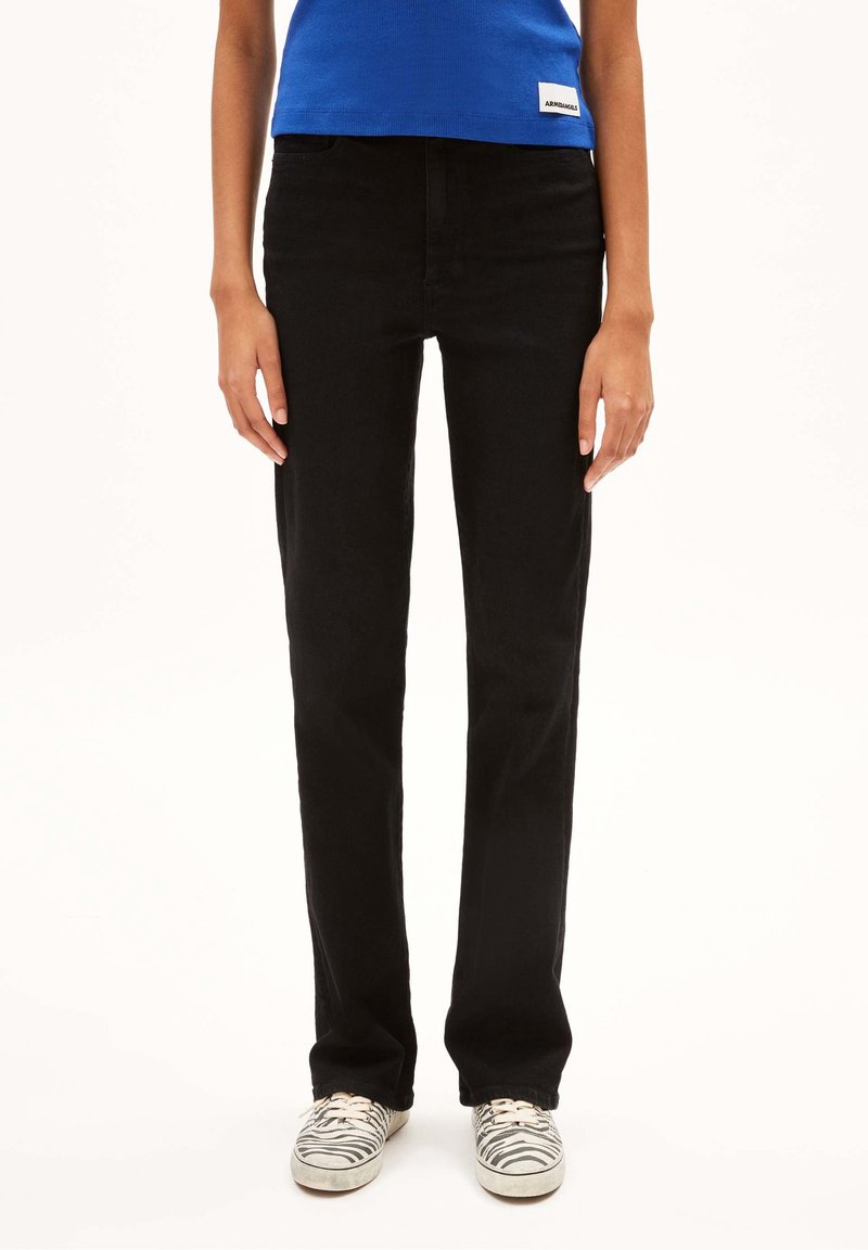 Mustat farkut suoran lahkeen leikkauksella, keskikorkealla vyötäröllä, viiden taskun suunnittelulla ja sileällä pinnalla, yhdistettynä seepra-kuosisilla lenkkareilla.