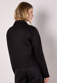 Czarna krótka kurtka z usztywnianym kołnierzem i długimi rękawami. Wykonana z fakturowanej tkaniny, z przeszyciami i mankietami na guziki.