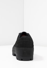 Czarny zamszowy niskoprofilowy sneaker z gumową podeszwą, z zaokrąglonym noskiem, wyściełanym kołnierzem i logo na obszarze pięty. Teksturowany i smukły design.