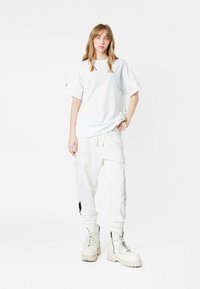 Camiseta blanca oversized con cuello redondo, combinada con pantalones blancos ajustados que presentan bordados laterales, y botas blancas de cordones gruesos.
