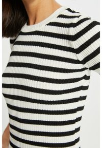 Schwarz-weiß gestreiftes, geripptes Strickoberteil mit rundem Ausschnitt und kurzen Ärmeln, das einen strukturierten Stoff zeigt.