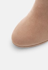 Pointe de chaussure en daim beige avec une forme arrondie et une texture lisse, présentée sur un fond clair uni.