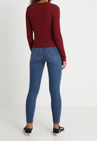 Musta pitkähihaine paita ja siniset tiukat farkut, joissa on sileä kangas, tiukka malli ja kaksi takataskua. Mustat lenkkarit viimeistelevät asun.