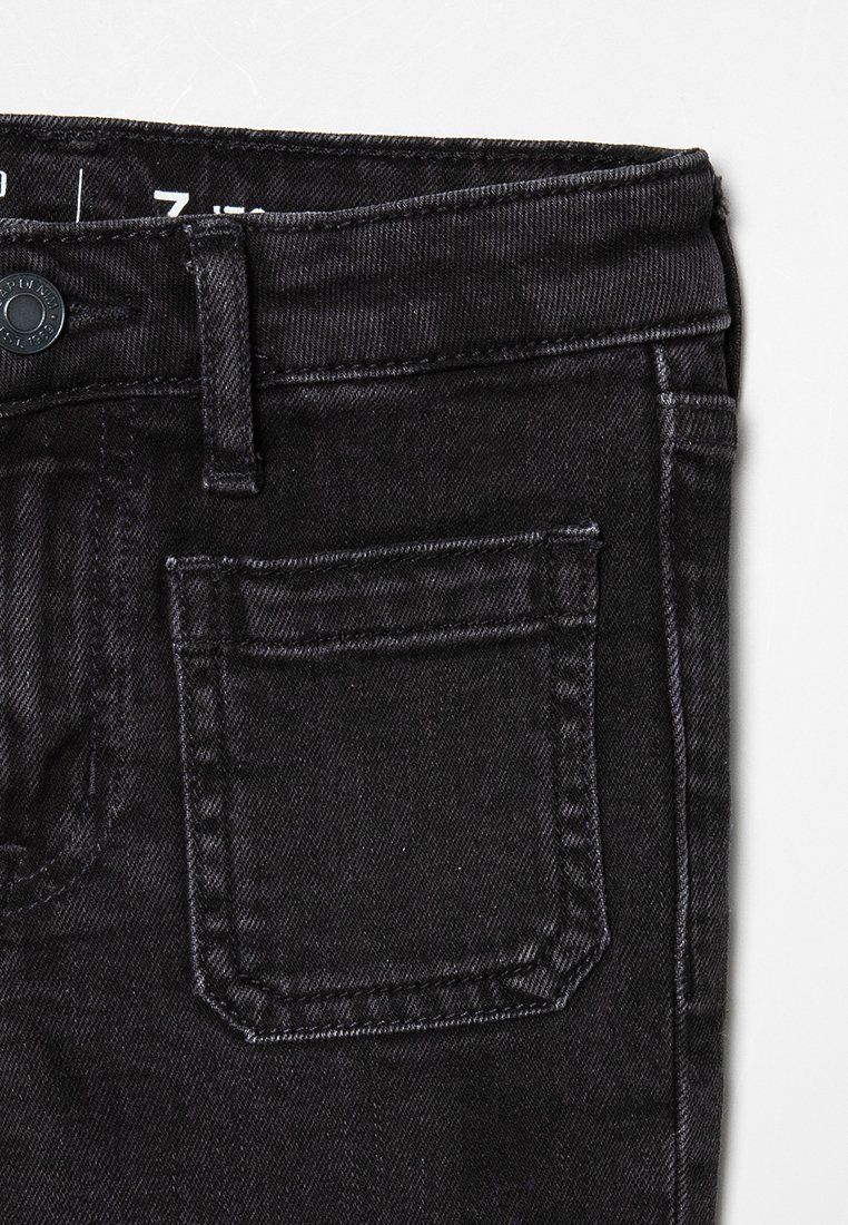 Gros plan sur un jean en denim noir, avec une taille standard, une petite poche arrière et une texture subtile agrémentée de détails de couture.