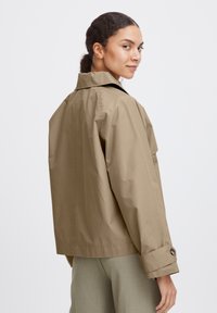 Giacca corta di colore khaki, resistente all'acqua, con colletto, polsini abbottonati e vestibilità morbida, che presenta una texture liscia e raffinata.