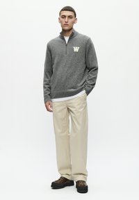 Gray zip-neck sweater made of knit material with a white "W" logo, paired with light beige pants and dark brown hiking boots.