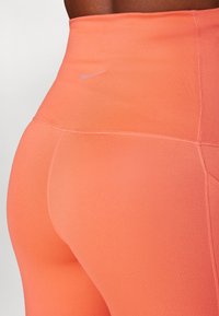 Høytlivde leggings i lys korall stoff med jevn tekstur. Nike-logo i lysegrått, med sømmer og en tettsittende design.