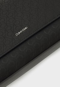Svart syntetisk totebag med teksturert mønster, subtil Calvin Klein-logo, og glatte læraktige detaljer. Kompakt og strukturert design.