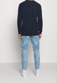 Granatowa prążkowana koszula z długim rękawem w połączeniu z jasnoniebieskimi dżinsami z wytłaczanymi wzorami, uzupełniona białymi trampkami.