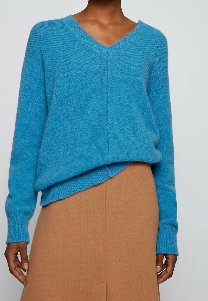 Pull tricot bleu doux avec col en V et épaules tombantes. Caractérisé par une coupe décontractée et des poignets côtelés, associé à une jupe beige.