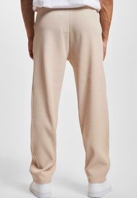 Pantalones de canalé beige con un ajuste relajado, que presentan una textura suave y líneas verticales, combinados con zapatillas blancas.
