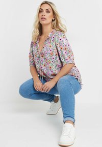 Blommig blus med flerfärgad mönster, korta ärmar, spetskrage, matchad med ljusblå jeans och vita sneakers. Har en lös passform.