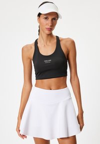 Svart sport-bh med texten "FEELING GOOD", i kombination med en vit, utsvängd träningskjol. Mjuk, elastisk tyg; atletisk passform och design.