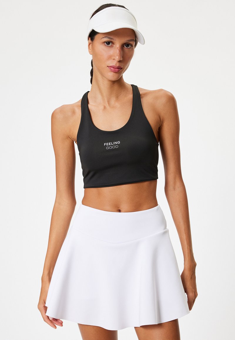 Svart sport-bh med texten "FEELING GOOD", i kombination med en vit, utsvängd träningskjol. Mjuk, elastisk tyg; atletisk passform och design.