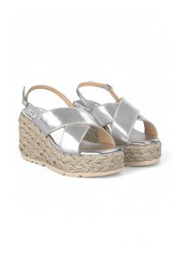 Silbermetallische Wedgesandalen mit einer geflochtenen Juteplattform, Überkreuzgurt-Design, offener Zehenbereich und verstellbarem Knöchelriemen.