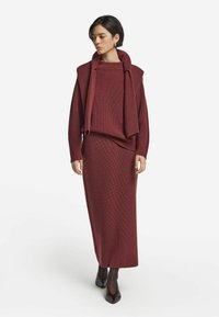 Ribbade stickade matchande set i djupt vinröd; oversized tröja med draperad krage och lång kjol; matchas med svarta klackskor.