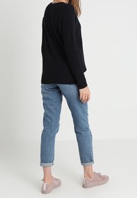 Schwarzer Strickpullover kombiniert mit hellblauen, umgeschlagenen Jeans und rosa Wildledersneakern. Keine sichtbaren Muster. Einfaches Design und Textur.