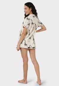 Conjunto de pijama beige con mangas cortas y pantalones cortos, que presenta un estampado de jirafa negra y detalles de acento en las mangas. Tejido suave y ligero.
