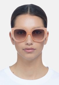 Gafas de sol de color melocotón de gran tamaño con montura cuadrada, lentes degradados y un acabado de plástico suave. Los detalles claros realzan el diseño moderno.