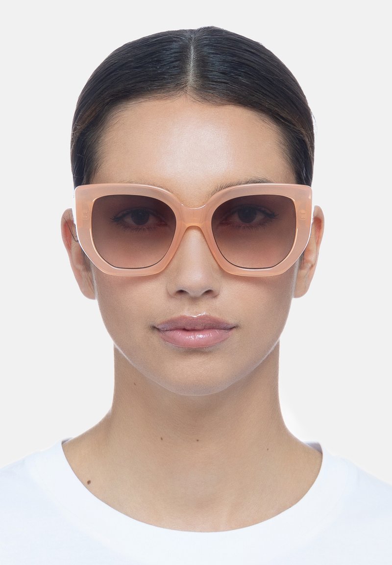 Gafas de sol de color melocotón de gran tamaño con montura cuadrada, lentes degradados y un acabado de plástico suave. Los detalles claros realzan el diseño moderno.
