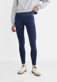 Leggings de canalé en color azul marino con cintura alta. El material es elástico y ajustado. Se llevan con una sudadera gris y zapatillas blancas.