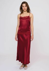 Abito sottoveste in satin rosso con bordi in pizzo sul décolleté e sull'orlo, caratterizzato da spalline sottili e una silhouette morbida e fluida.