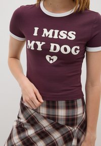 Camiseta color burdeos con cuello blanco y mangas cortas, que presenta el texto "ECHO DE MENOS A MI PERRO" y un pequeño icono de perro en forma de corazón.