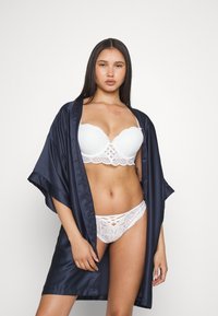 Kimono en satin marine avec de larges manches, porté sur un soutien-gorge en dentelle blanche et un string assorti, présentant des motifs complexes et des détails découpés.
