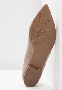 Semelle d'une chaussure à bout pointu en daim beige montrant des motifs de pièces embossées, le texte "KAISER", la taille 4½, et le logo "PK" sur le talon.