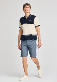Marinblå och krämrandig polo med korta ärmar, kombinerad med ljusblå shorts och vita sneakers. Avspänt snitt och mjuk textur.