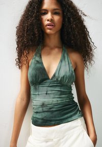Green tie-dye halter top with ruched texture and plunging neckline. Features soft, stretchy fabric. Paired with light-colored trousers.
