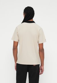 Short-sleeved beige polo shirt with a black collar. Smooth fabric with a tag at the hem. Simple design, suitable for casual wear.
