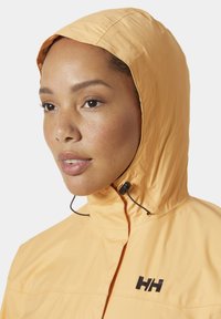 Chaqueta de lluvia ligera amarilla con capucha, que presenta un cuello alto, cordón ajustable y un logo negro en el pecho. Textura suave.