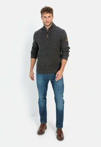 Grauer Zip-Up-Pullover mit strukturiertem Strick, gerippten Bündchen und einem Lederakzent am Ärmel, kombiniert mit blauen Jeans und braunen Schuhen.