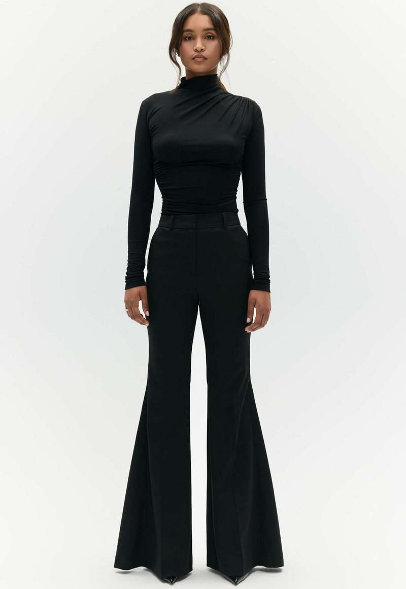 Zwarte turtleneck top met plooidetails, gecombineerd met zwarte high-waisted broek met wijde pijpen, kenmerkend door een soepele textuur en subtiele glans.