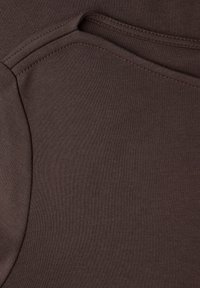 Bruine katoenen stof met een gladde textuur en een geribbeld patroon, met een gevouwen naad. Eenvoudige, effen kleur zonder extra accenten.