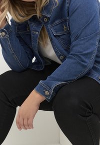 Denimjakke i mørkeblå med tætsiddende design, knaplukning foran, brystlommer og knapmanchetter, kombineret med sorte jeans.