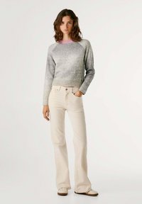 Jersey de punto gris y rosa con escote redondo, combinado con jeans beige claros de campana y zapatillas beige. Texturas suaves y silueta entallada.
