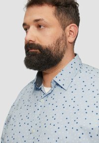 Lichtblauw overhemdd-shirt met een verspreid stippenpatroon in verschillende tinten blauw. Met een kraag en een contrasterende donkergrijze kraag.