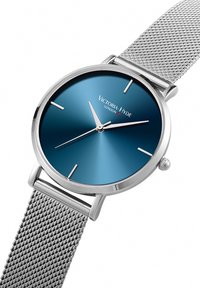 Orologio da polso in rete argentata con quadrante rotondo di un blu profondo, indicatori minimalisti e lancette delle ore e dei minuti sottili. Logo del produttore al centro.
