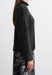 Pull en maille gris foncé avec un col montant, un ourlet côtelé et des épaules tombantes, associé à une jupe à motifs avec des détails floraux.