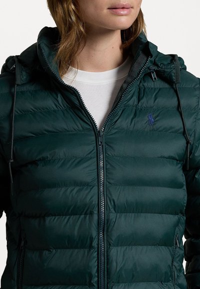 Donkergroene pufferjack met een capuchon, voorzien van een ritssluiting aan de voorkant, horizontale stiknaden en een klein blauw logo aan de linkerkant.